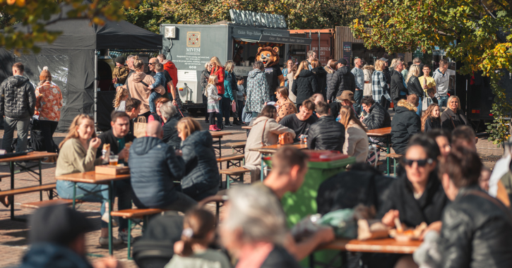 crowds sitting eating and drinking on benches with food trucks in background at Chester-le-eats food festival